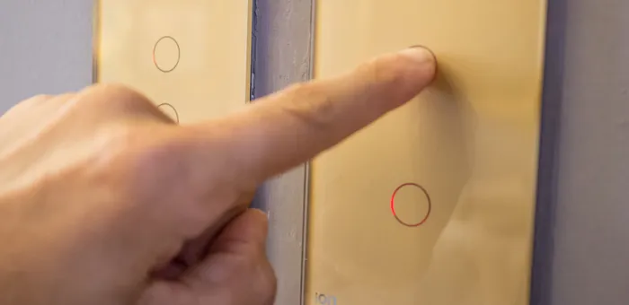 Mano presionando interruptor ION Glass dorado — experiencia touch en acabado champagne