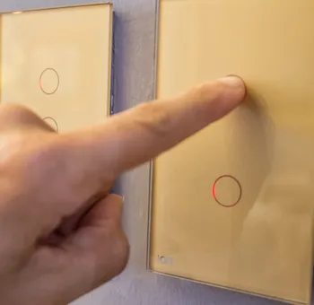 Mano presionando interruptor ION Glass dorado — experiencia touch en acabado champagne