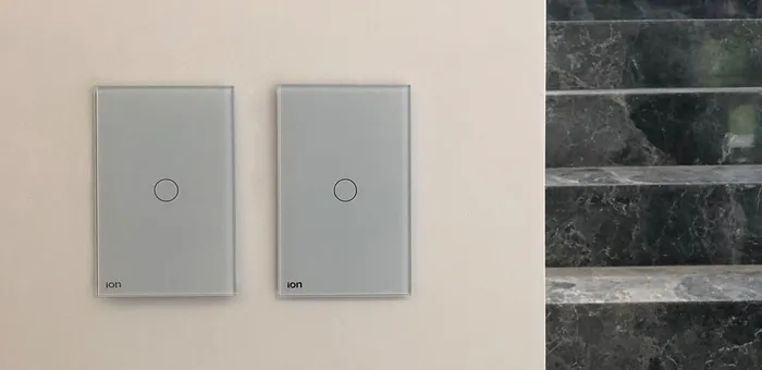 Interruptores ION Glass grises instalados en pared con escalera de mármol — ambiente residencial de lujo