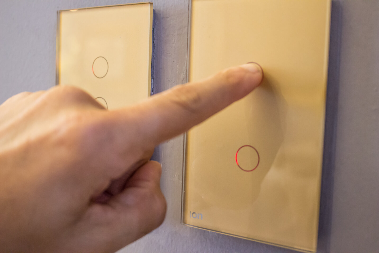 Mano presionando interruptor ION Glass dorado — experiencia touch en acabado champagne