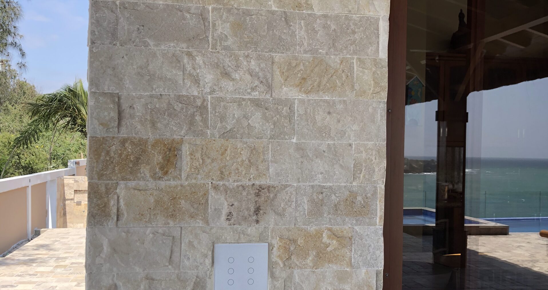 Interruptor ION Glass instalado en pared de travertino — exterior de residencia de lujo con vista a piscina