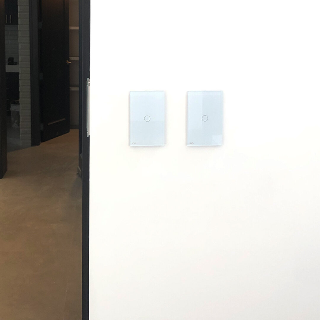 Interruptores ION Glass blancos instalados en pared blanca — espacio contemporáneo con puerta de vidrio