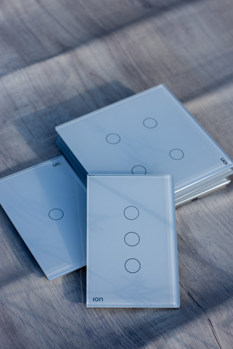 Interruptores ION Glass blancos apilados sobre superficie de madera — línea simple disponible en 4 acabados