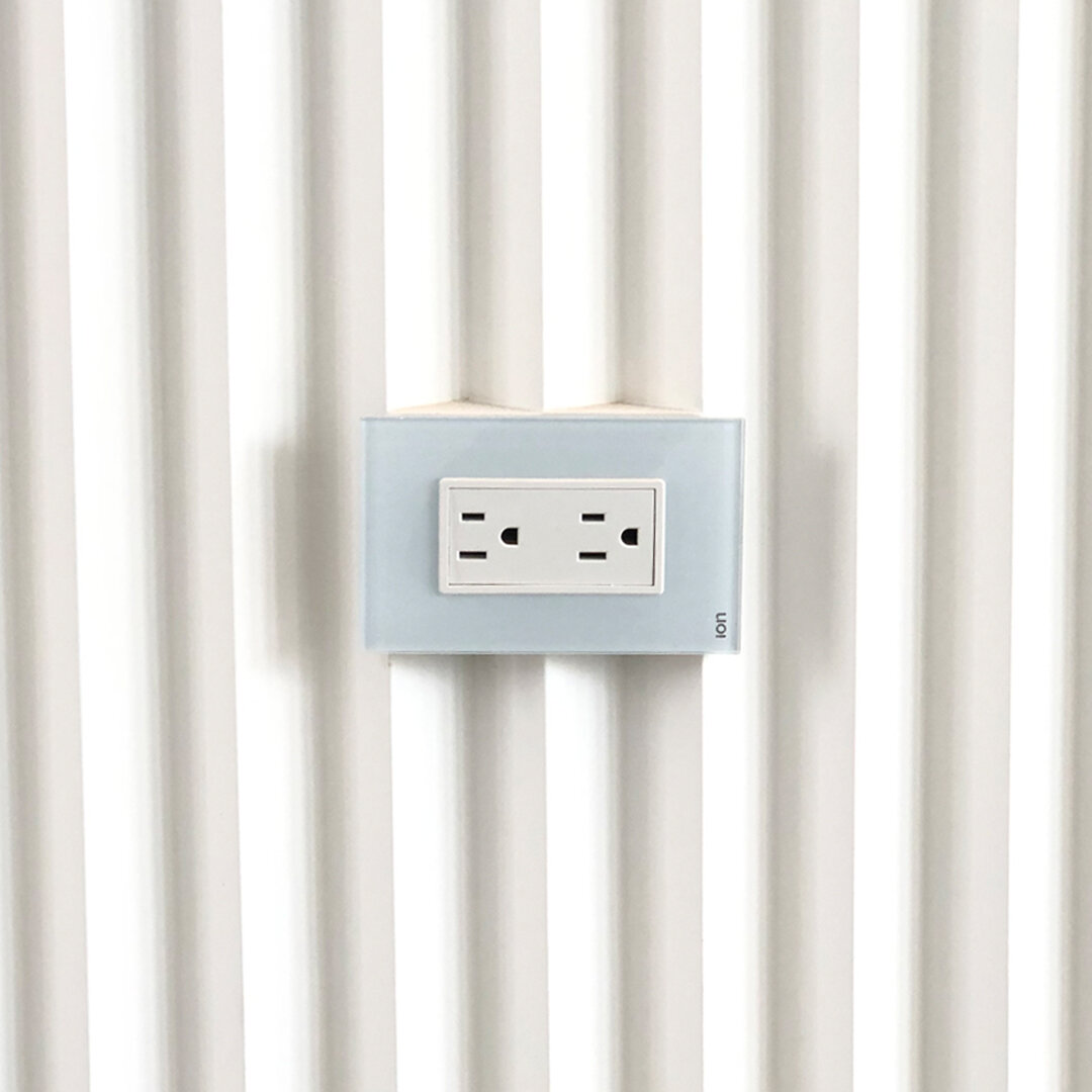 Tomacorriente ION Glass blanco en pared acanalada — panel de vidrio templado acabado premium